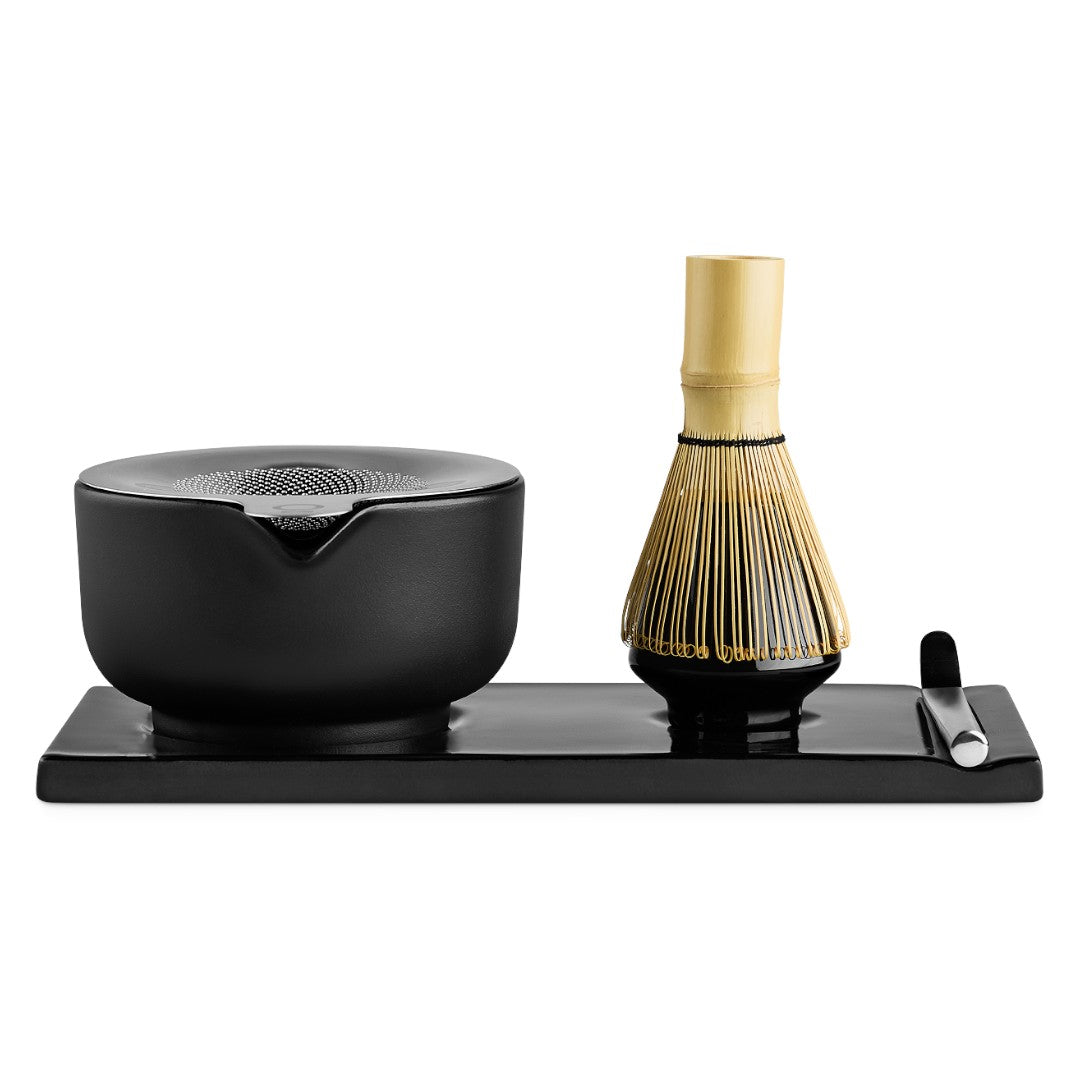 Fellow black ceramic matcha whisk set on a rectangular black tray, featuring a bamboo-handled whisk, a black bowl, and a small black-and-silver scoop, photographed on a white background.