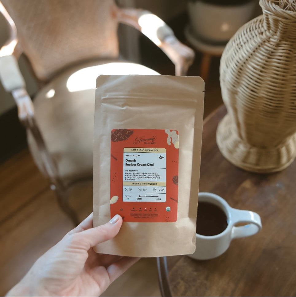 Hand holding a package of tea with a blurred background of a cozy room.